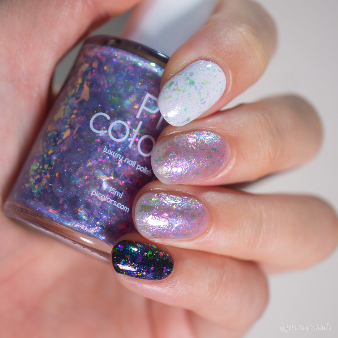 A hand with PI Colors Stained Glass.436 multicolored, iridescent flakie polish holds a bottle of purple-grey polish. Each nail shows the handmade polish’s unique shimmer over white, pink, natural, and black bases.