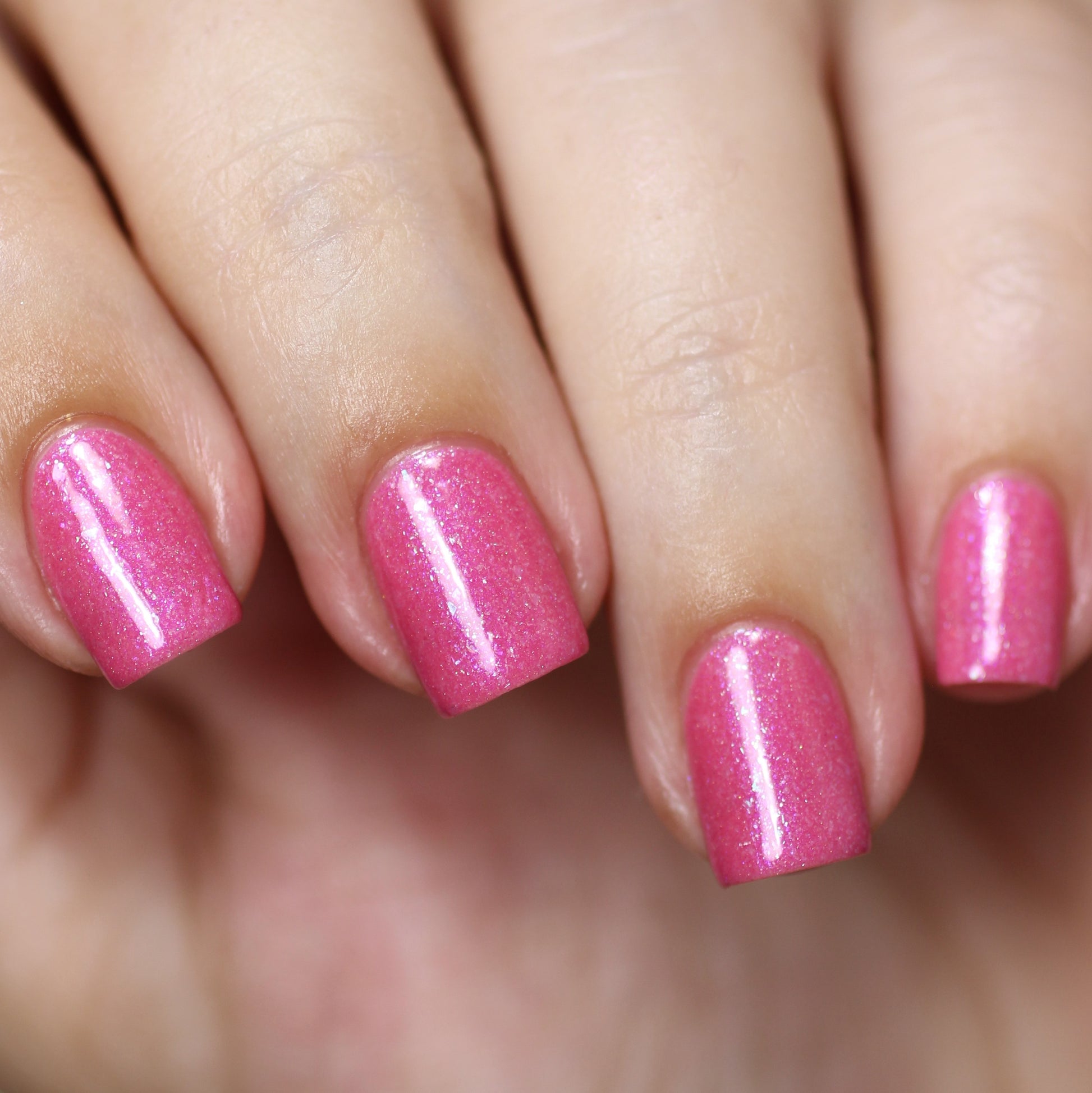 A close-up shot showcases a hand flaunting impeccably manicured nails adorned with PI Colors' Strawberry Sundae.002 Pink Nail Polish, a handcrafted product featuring vibrant, glittery pink shades. The polish catches the light like holographic powder, imparting a lustrous finish to the nails.