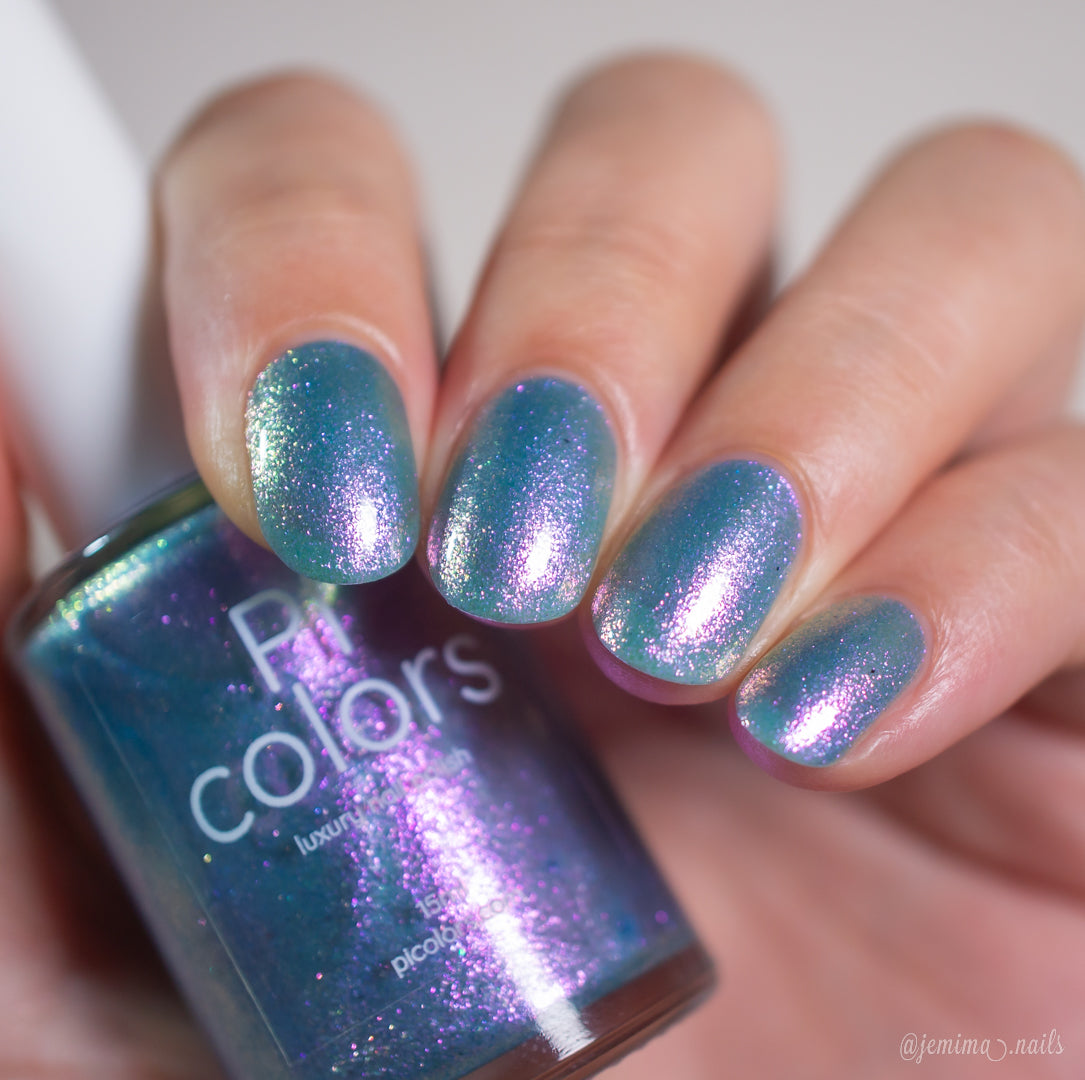 A hand with medium-length, rounded nails painted in PI Colors Sugar Sparkles.451—a shimmery teal polish with pink and purple iridescence—holds the matching bottle.