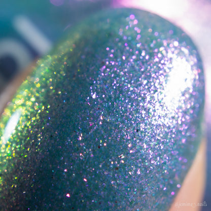 Close-up of a fingernail painted with PI Colors Sugar Sparkles.451, a luxury lacquer showing iridescent blue, purple, green, and pink glitter sparkling under bright light.