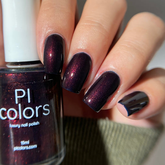 Nail polish bottle with dark purple nail polish on nails, against a neutral background