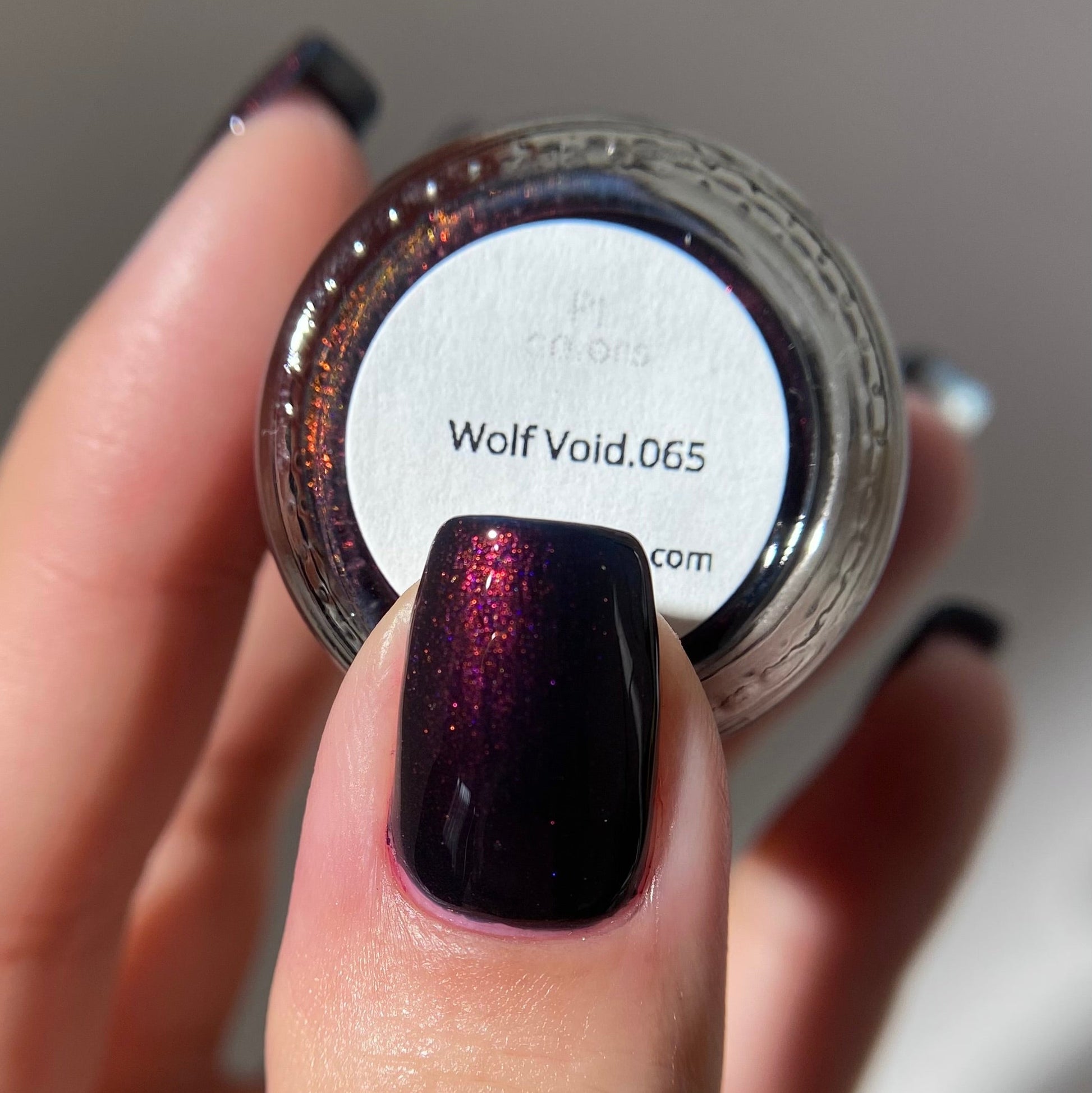 Nail polish jar labeled 'Wolf Void.065' with a hand holding a dark glittery nail.