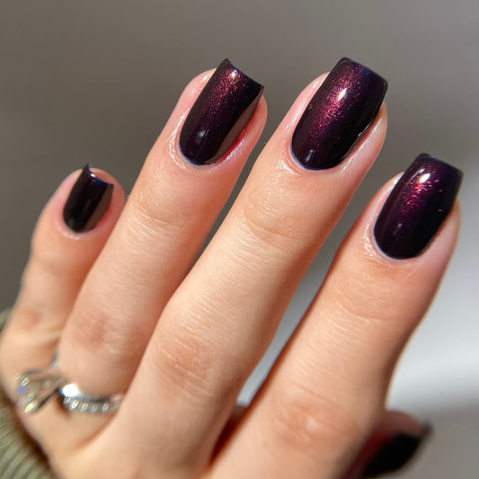 Hand with dark purple nail polish on a neutral background