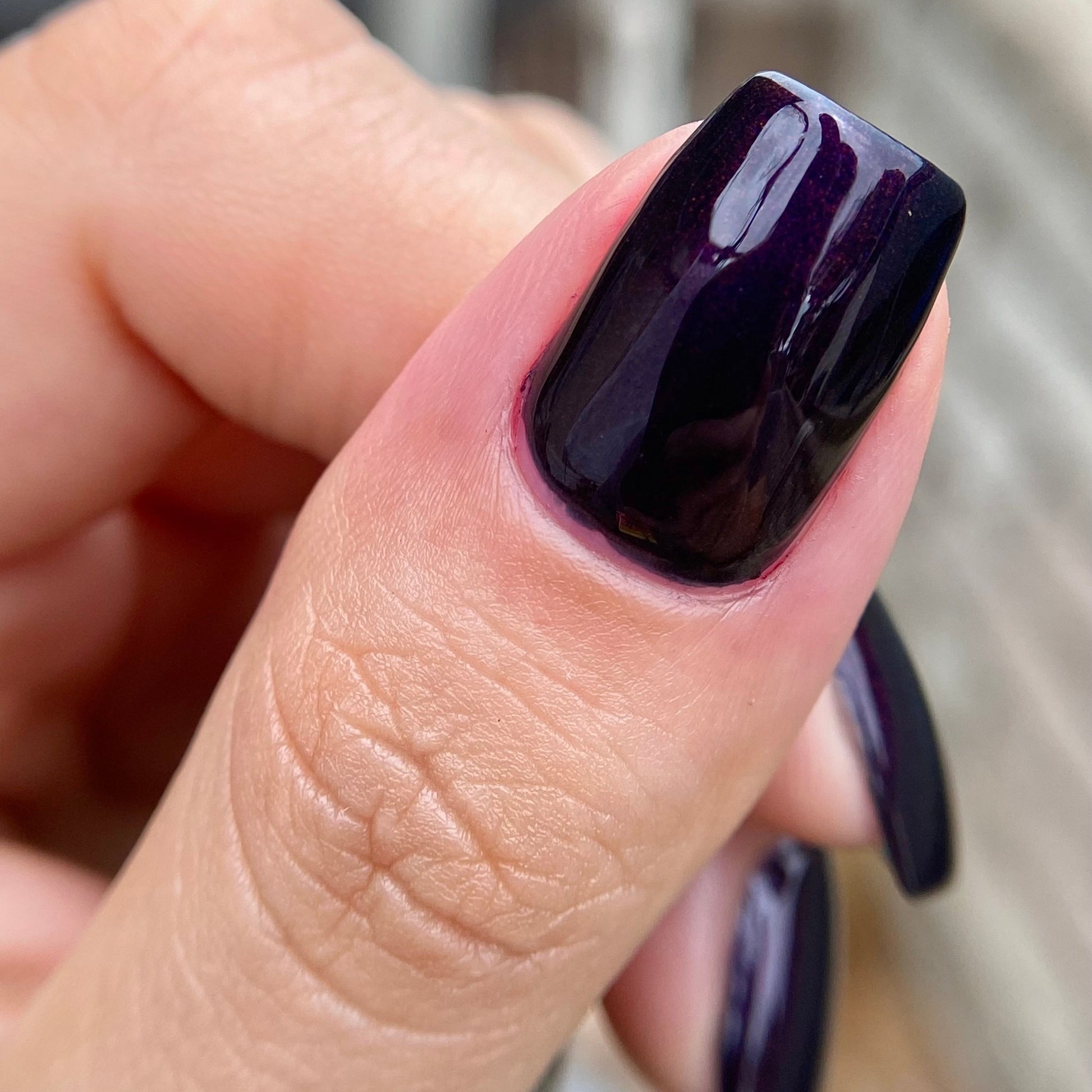 Close-up of a hand with dark purple nail polish on a blurred background
