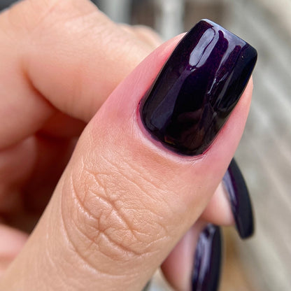 Close-up of a hand with dark purple nail polish on a blurred background
