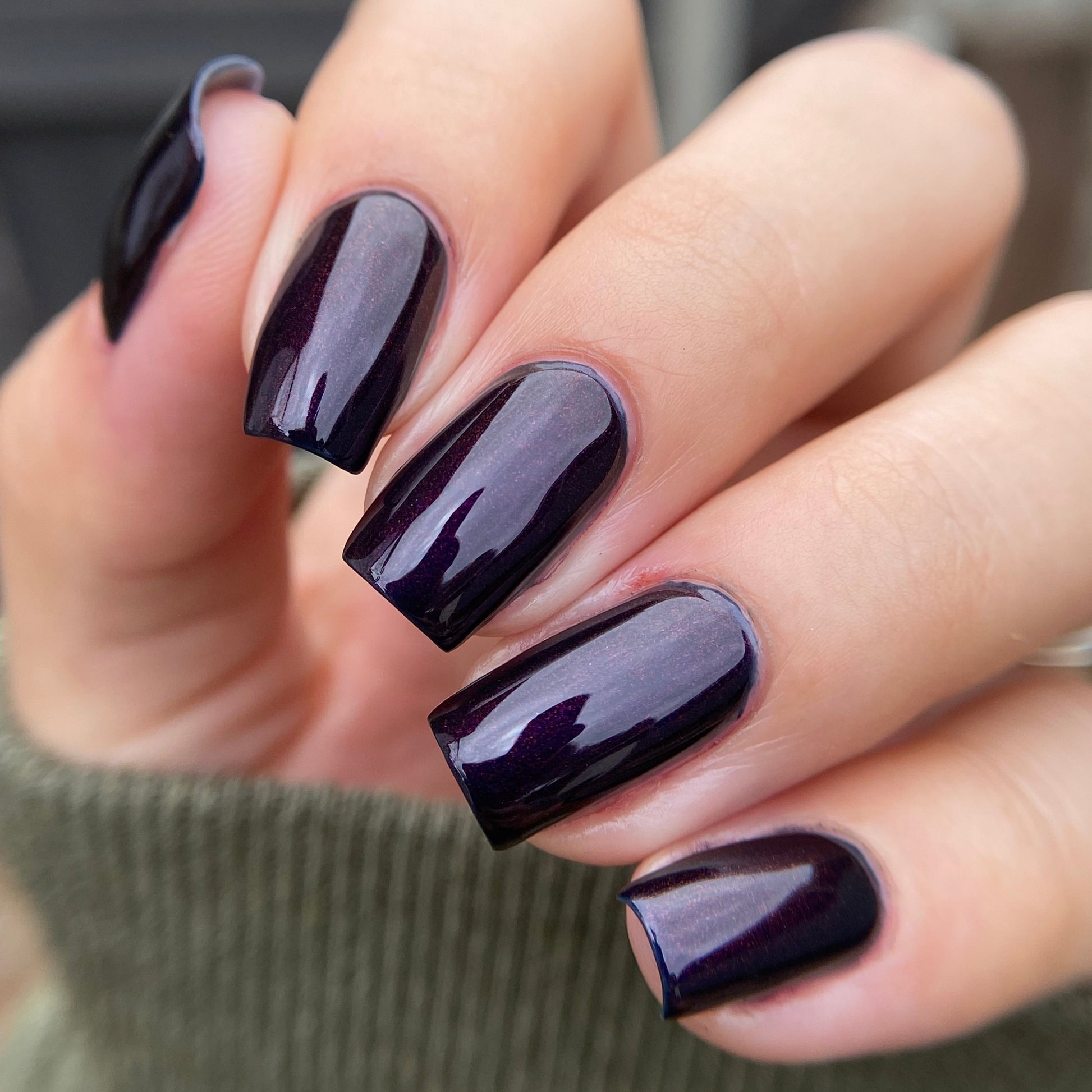 Close-up of a hand with dark purple nail polish on a blurred background