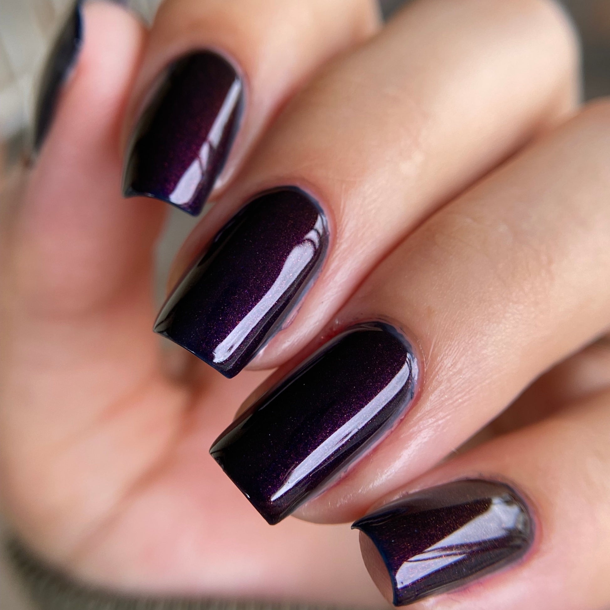 Close-up of a hand with dark purple nail polish on a blurred background