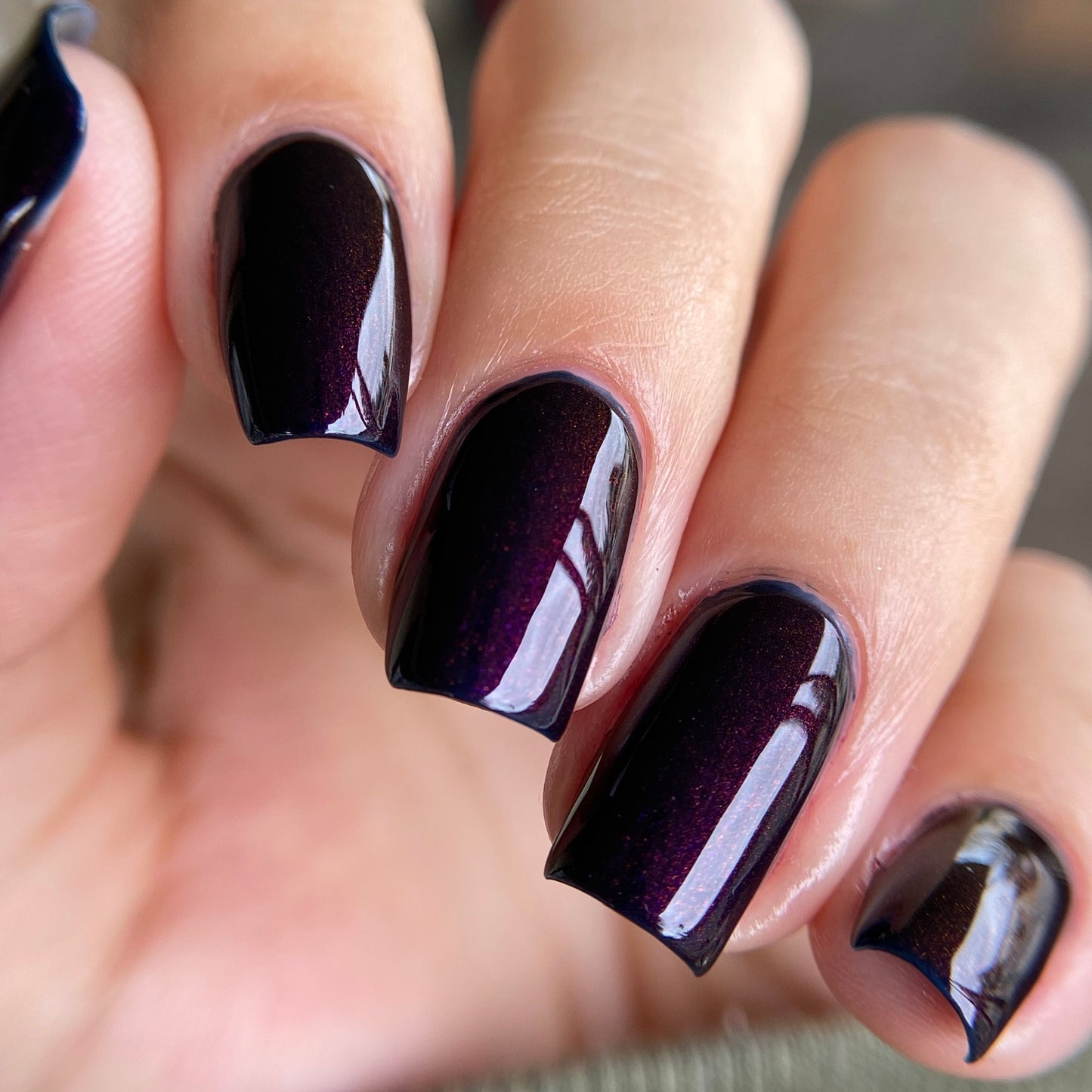 Close-up of a hand with dark purple nail polish on a blurred background
