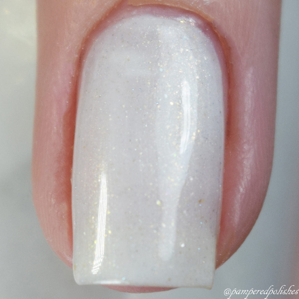 A close-up of a fingernail adorned with PI Colors' Aurum Dust.069 White Nail Polish reveals a glossy and sparkling finish. This luxurious nail lacquer, with its subtle glitter particles that catch the light, exemplifies opulent elegance in the craftsmanship of handmade nail polish.