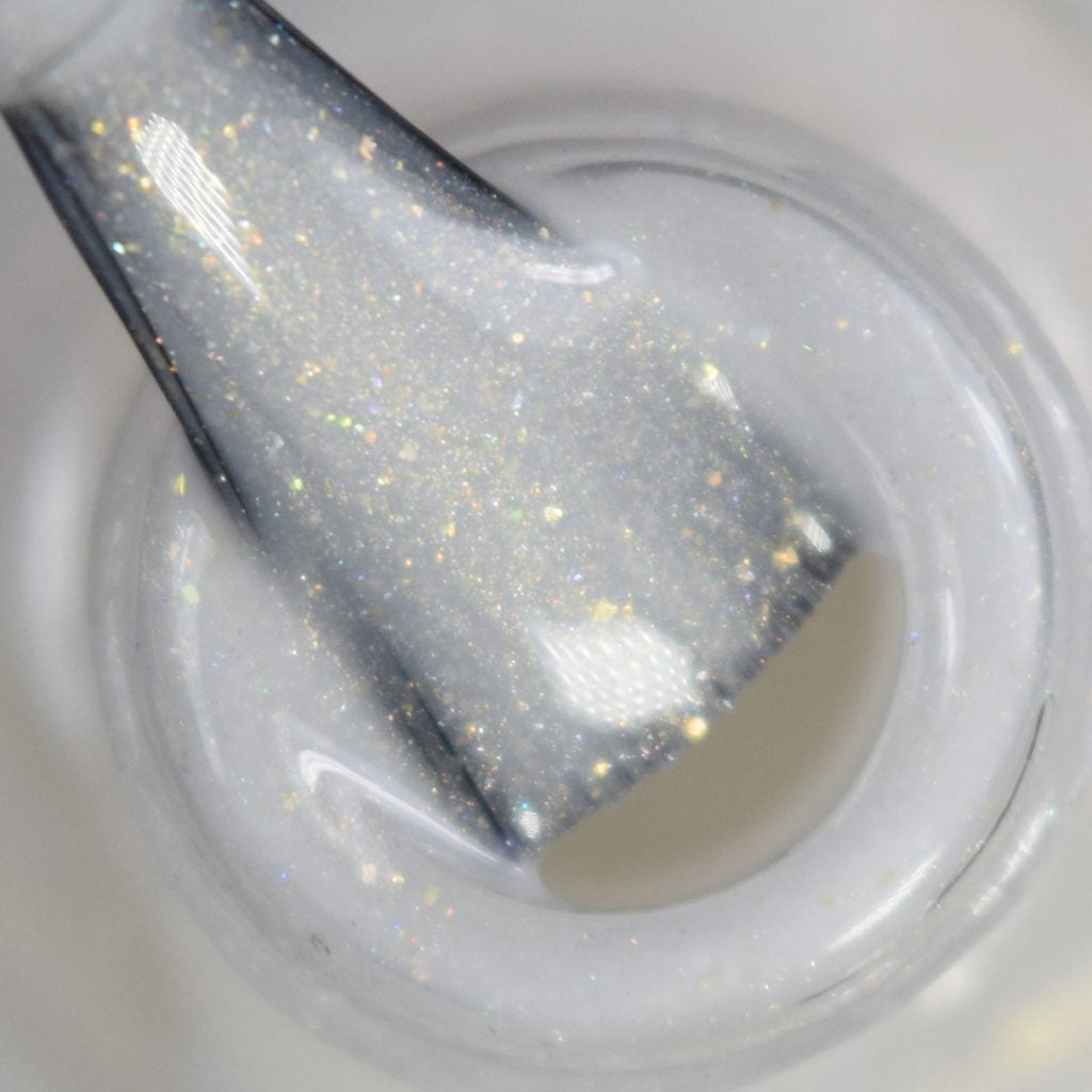 A close-up of a nail polish brush immersed in PI Colors' Aurum Dust.069 White Nail Polish, revealing its shimmery, pearlescent finish. The glossy texture highlights fine glitters that reflect light in a spectrum of colors, reminiscent of the enchanting sparkle associated with Aurum Dust.069.