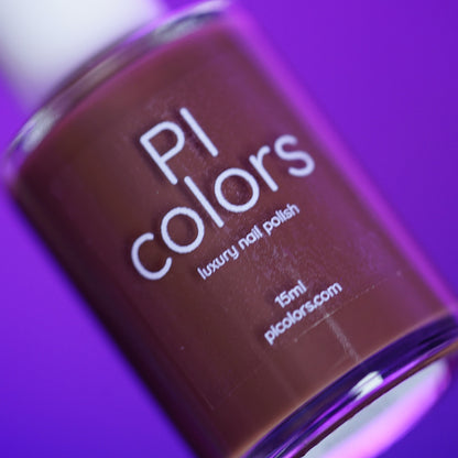 A close-up of PI Colors’ Chocolate Turtle.411, a handmade chocolate brown creme nail polish, displayed against a vibrant purple background. The bottle label reads "PI Colors luxury nail polish 15ml picolor.com.