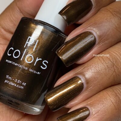 A close-up of a hand with long nails painted in the luxurious "Eclair.001 Brown" shade exudes elegance. The person holds a bottle from PI Colors, showcasing the same rich hue.