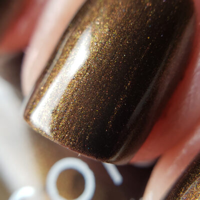 A close-up of a fingernail painted with PI Colors' Eclair.001 Brown Nail Polish, showcasing its dark chocolate shade with a shimmery metallic finish and subtle undertones of gold and green that beautifully catch the light.