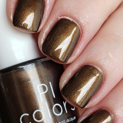 Close-up of nails adorned with the metallic shimmer of Eclair.001 Brown Nail Polish, positioned beside a bottle labeled "PI Colors." This luxurious lacquer is known for its glossy finish that captures and reflects light. The light skin tone accentuates the deep, rich shade created through artisanal techniques.