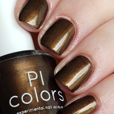 A close-up displays a hand with nails painted in a glossy, dark chocolate brown shade. The thumb holds a bottle of PI Colors' Eclair.001 Brown Nail Polish, emphasizing its experimental and handcrafted charm in the same hue.