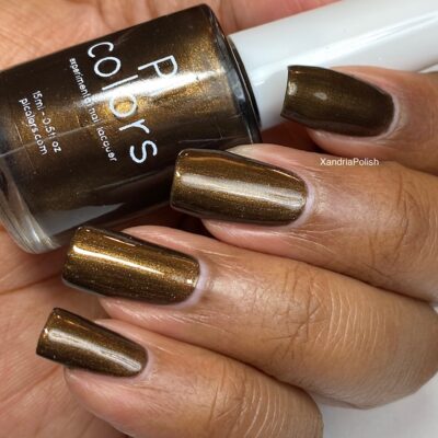 A close-up features a hand flaunting long, glossy nails adorned with Eclair.001 Brown Nail Polish by PI Colors, in a luxurious metallic bronze hue. The bottle is held snugly between the fingers, revealing its label and suggesting a hint of dark chocolate brown with a shimmering, reflective finish.