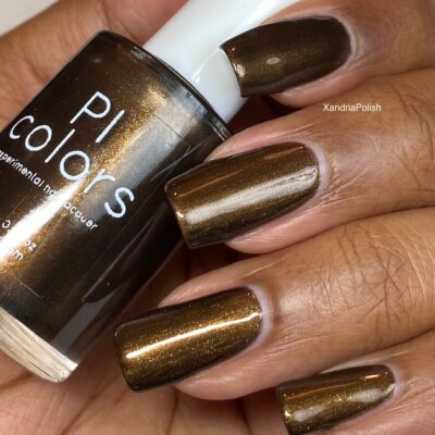 A close-up shot captures a hand adorned with Eclair.001 Brown Nail Polish by PI Colors, holding the chic bottle of this luxury nail lacquer. The scene is well-lit, highlighting the polish's shimmery and smooth finish, evocative of a sumptuous dark chocolate brown.