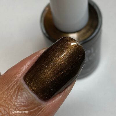 Close-up of a fingernail coated with Eclair.001 Brown Nail Polish by PI Colors, showcasing its shimmery dark chocolate hue. In the background, a bottle of this luxury nail lacquer gleams invitingly.