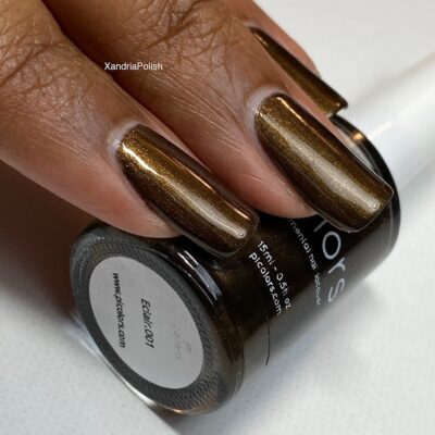 A close-up of a hand with long nails coated in shimmery Eclair.001 Brown Nail Polish holds a bottle from PI Colors. The rich hue beautifully catches the light, reminiscent of dark chocolate brown, adding an elegant touch to your look.