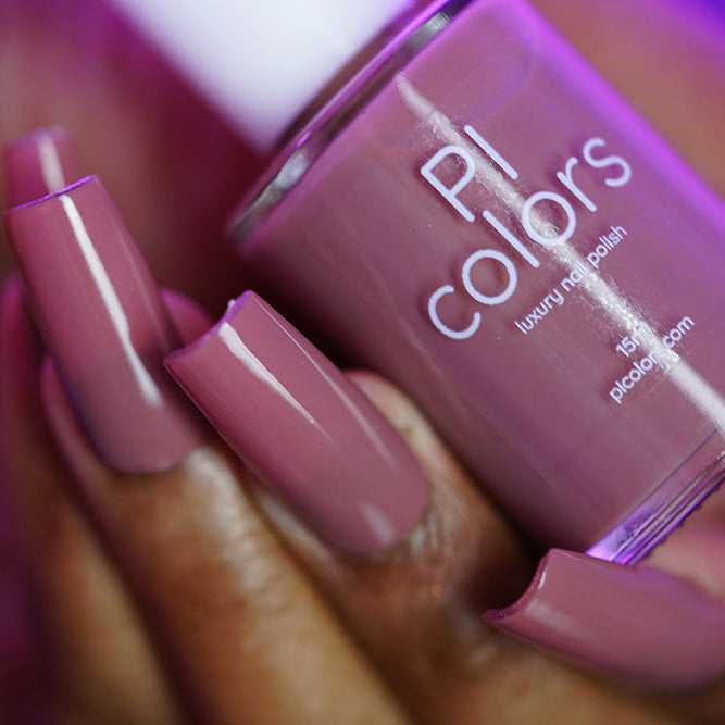 A hand with long, square-shaped nails painted in mauve pink holds a bottle of PI Colors Iced Oatmeal.478 10-free, handmade nail polish in a matching shade.
