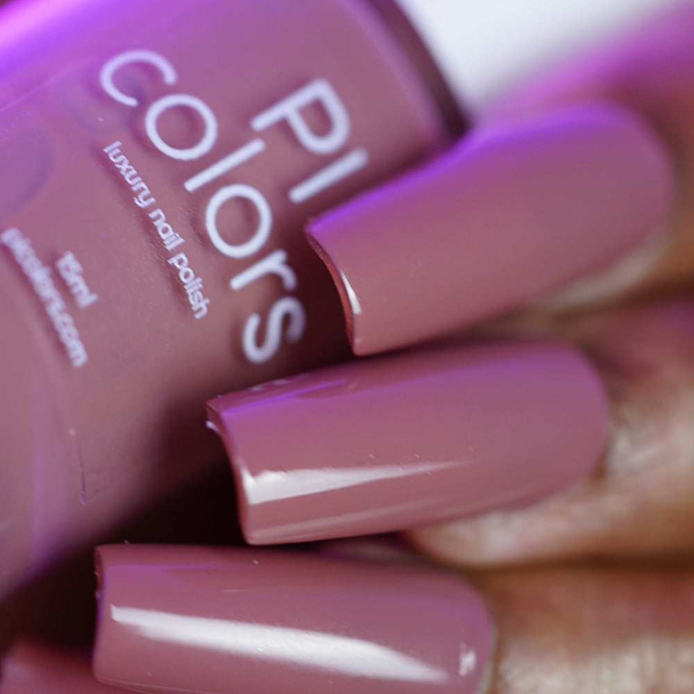 Close-up of a hand with long, glossy, mauve nails holding a matching "Iced Oatmeal.478" 10-free nail polish bottle from PI Colors.