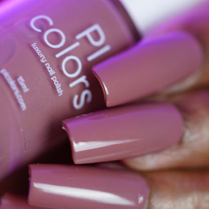 Close-up of a hand with long, glossy, mauve nails holding a matching "Iced Oatmeal.478" 10-free nail polish bottle from PI Colors.