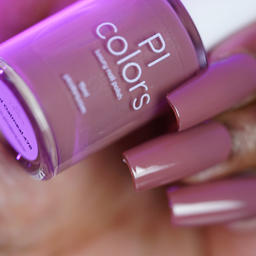 A hand with long, glossy mauve nails holds a matching bottle of PI Colors Iced Oatmeal.478 handmade nail polish.