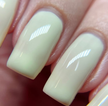 A close-up of fingers featuring glossy, pastel yellow nails reveals a neat, square-shaped manicure. The nails boast the creme finish of Chiffon.400 Yellow Nail Polish by PI Colors. Light reflections enhance the shiny effect and elegance on the nail surface.