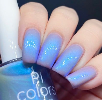 A hand with neatly manicured nails painted in a luxurious gradient of electric silver blue to purple, showcasing a soft shimmer and color-changing effects, holds a bottle of handmade nail polish labeled "Cloud Rainbow.303 Blue Nail Polish" by PI Colors.