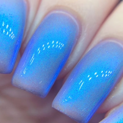 Close-up of nails with a gradient manicure transitioning from light purple to vibrant blue, featuring PI Colors' luxurious Cloud Rainbow.303 Blue Nail Polish. Subtle specks of glitter add a shimmering effect under the light.