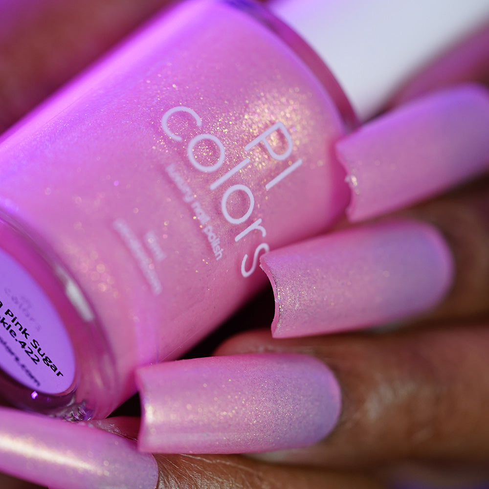 A close-up of a hand with long, square-shaped nails painted in shimmery pastel pink, holding a PI Colors Lemon Pink Sugar Cookie.422 handmade nail polish bottle labeled "Lemon Pink Sugar Cookie.422.