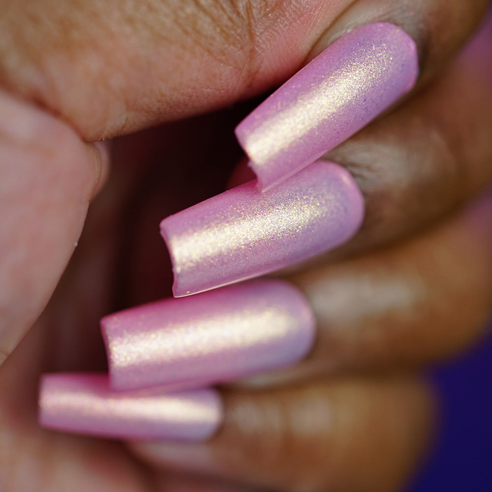 A close-up of a hand with long, square-shaped nails painted in PI Colors Lemon Pink Sugar Cookie.422, a shimmery pastel pink luxury lacquer, set against a blurred background.