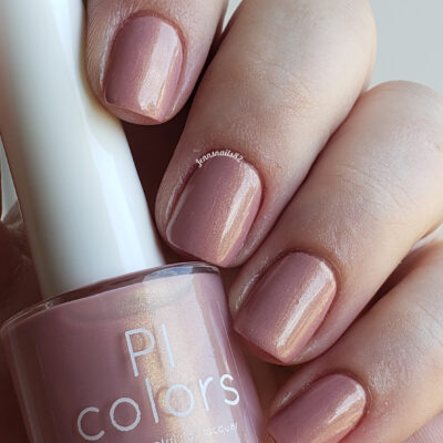 A close-up of a hand with nails painted in a glossy, muted pink shade conveys the essence of luxurious nail lacquers. Held between the fingers is a bottle of PI Colors' Milk Berry.073 Pink Nail Polish, perfectly matching the nail color against soft, neutral-toned skin.