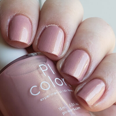 Close-up of a hand with neatly manicured nails painted in a glossy, muted pink shade. The nail polish bottle, labeled "PI Colors," is held in the other hand, displaying the same hue. This handmade nail polish epitomizes the elegance of luxury lacquers like Milk Berry.073 Pink Nail Polish.