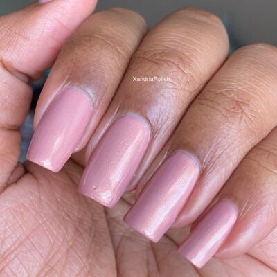 A close-up of a hand flaunting manicured nails painted in a soft, shimmery pink shade using Milk Berry.073 Pink Nail Polish from PI Colors.