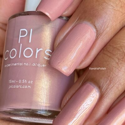 Close-up of a hand showcasing nails painted in a shimmery, pale pink nail polish. A bottle of the same luxury nail lacquer, labeled "Milk Berry.073 Pink Nail Polish by PI Colors," is held in the hand, displaying the shade on the label.
