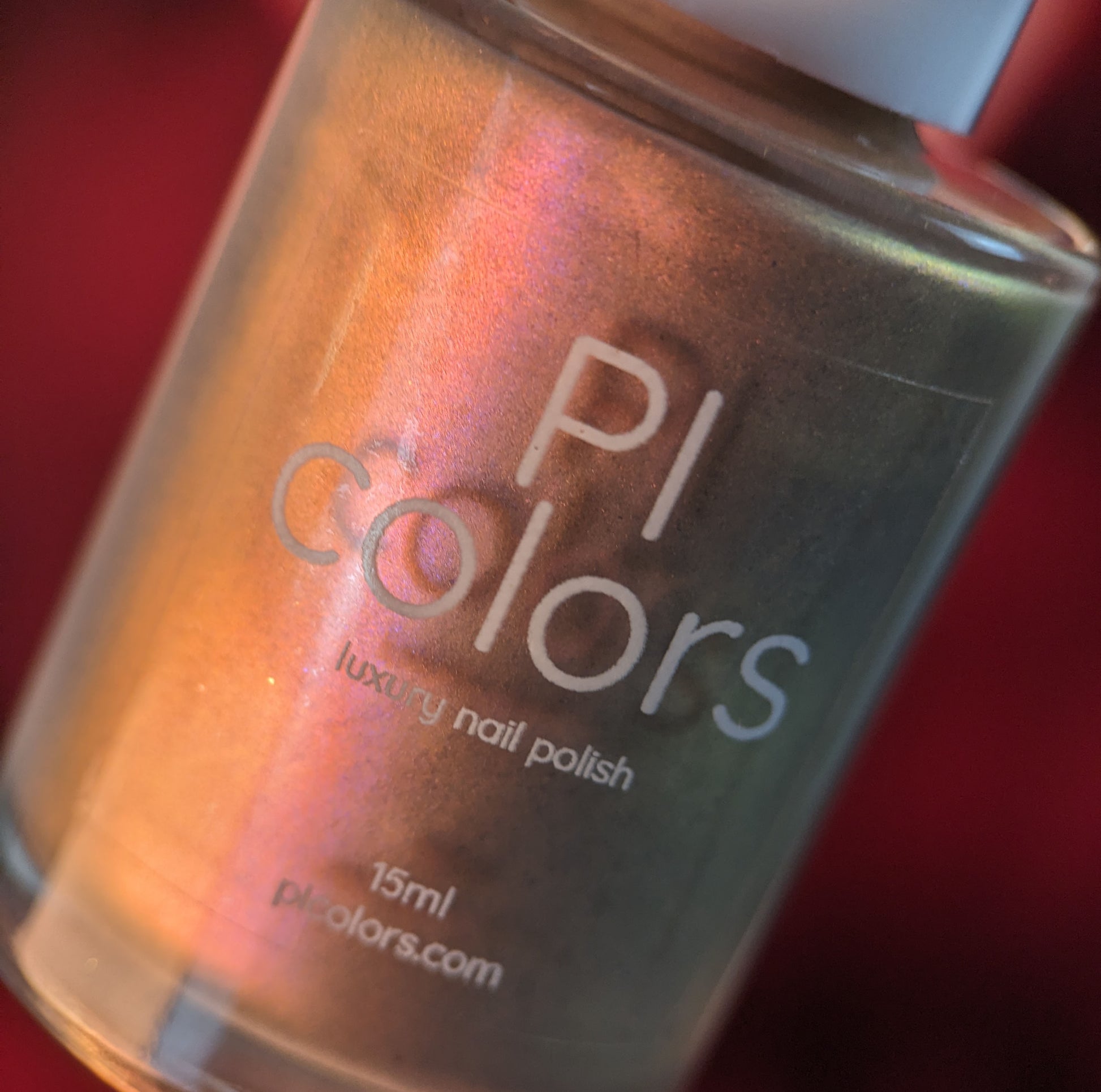 A close-up of a bottle of PI Colors luxury nail polish, Mulberry Love.205, reveals its handmade charm with a metallic sheen of orange, pink, and hidden bronze hues. The label displays "15ml" and "plcolors.com," highlighting its status among the finest luxury nail lacquers.