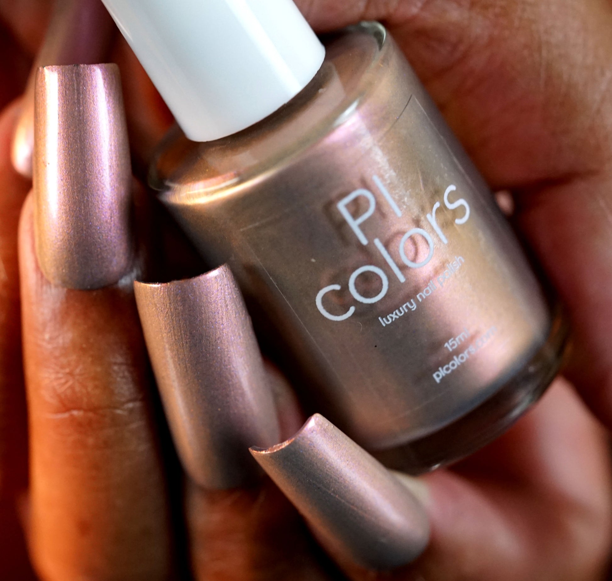 A close-up shows a hand holding PI Colors' Mulberry Love.205, a shimmery metallic nail polish that reflects the manicured nails. The luxurious bottle features a white cap and elegant front text.