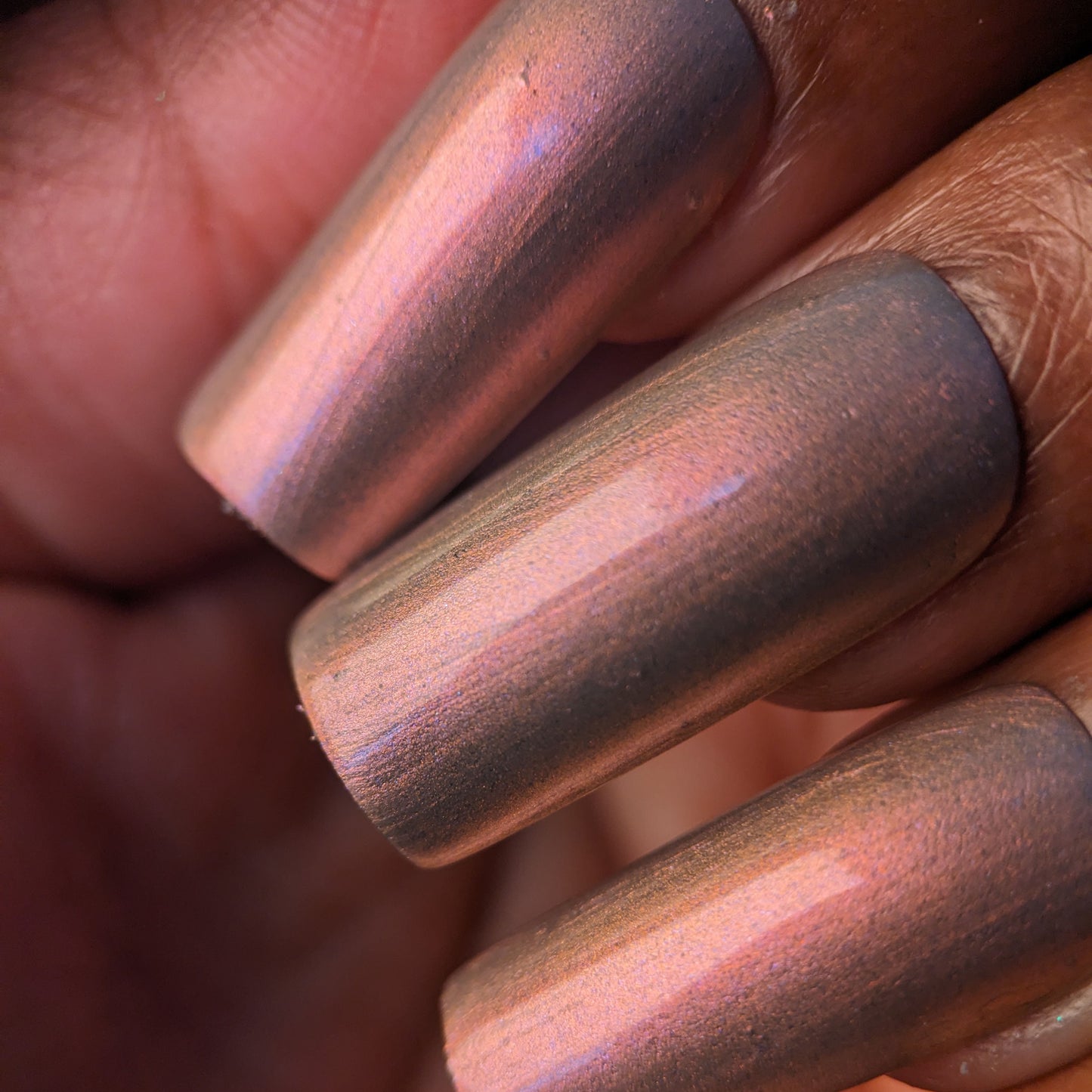 A hand adorned with PI Colors' Mulberry Love.205 displays a glossy, metallic multichrome polish in pink, purple, and gold hues. The luxurious bronze finish smoothly coats the nails, capturing the lighting to accentuate stunning color shifts.