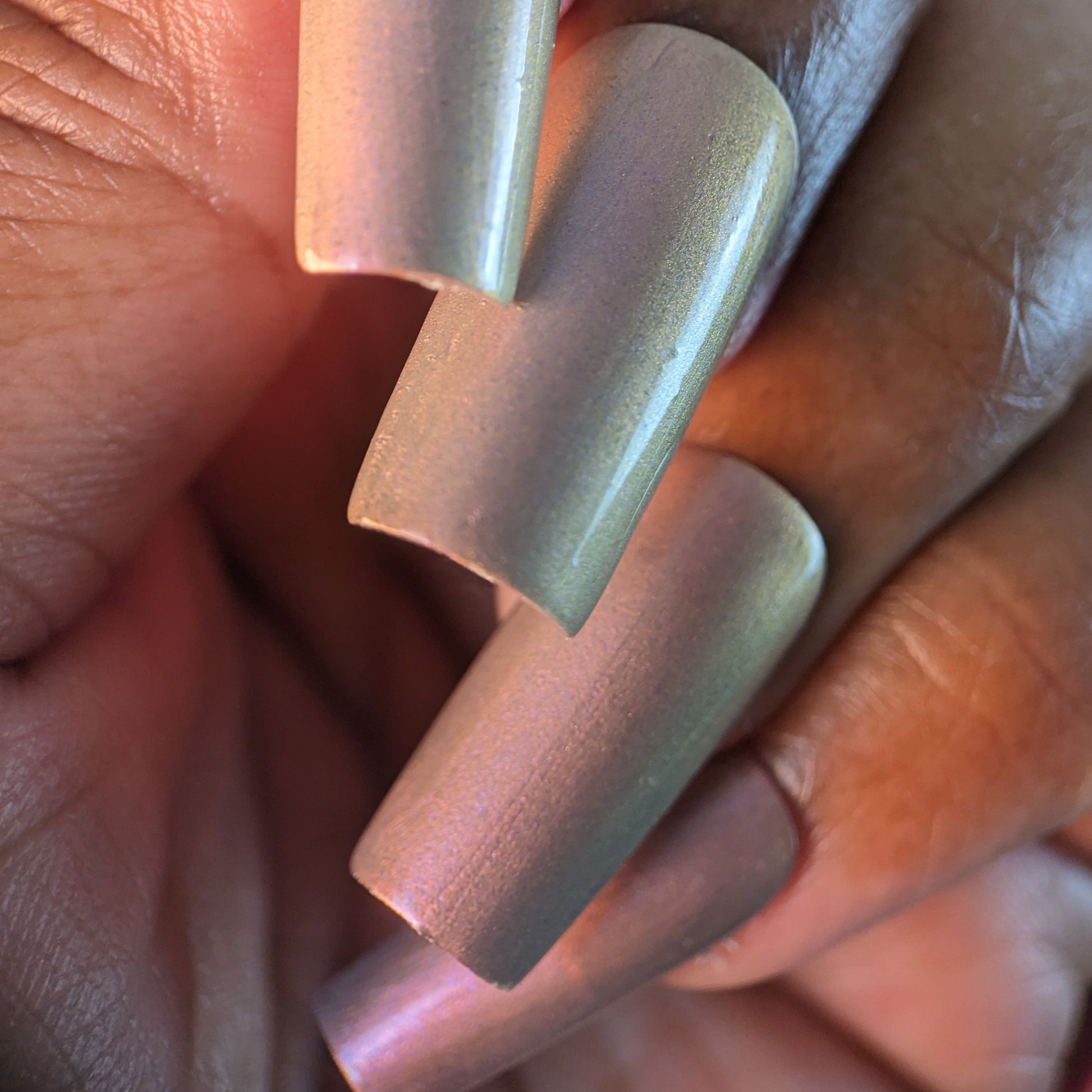 A hand with long, multichrome nails showcases a gradient of pink, gold, and green under lighting that highlights the glossy finish. This luxurious manicure is achieved with PI Colors' exquisite handmade nail polish, Mulberry Love.205.