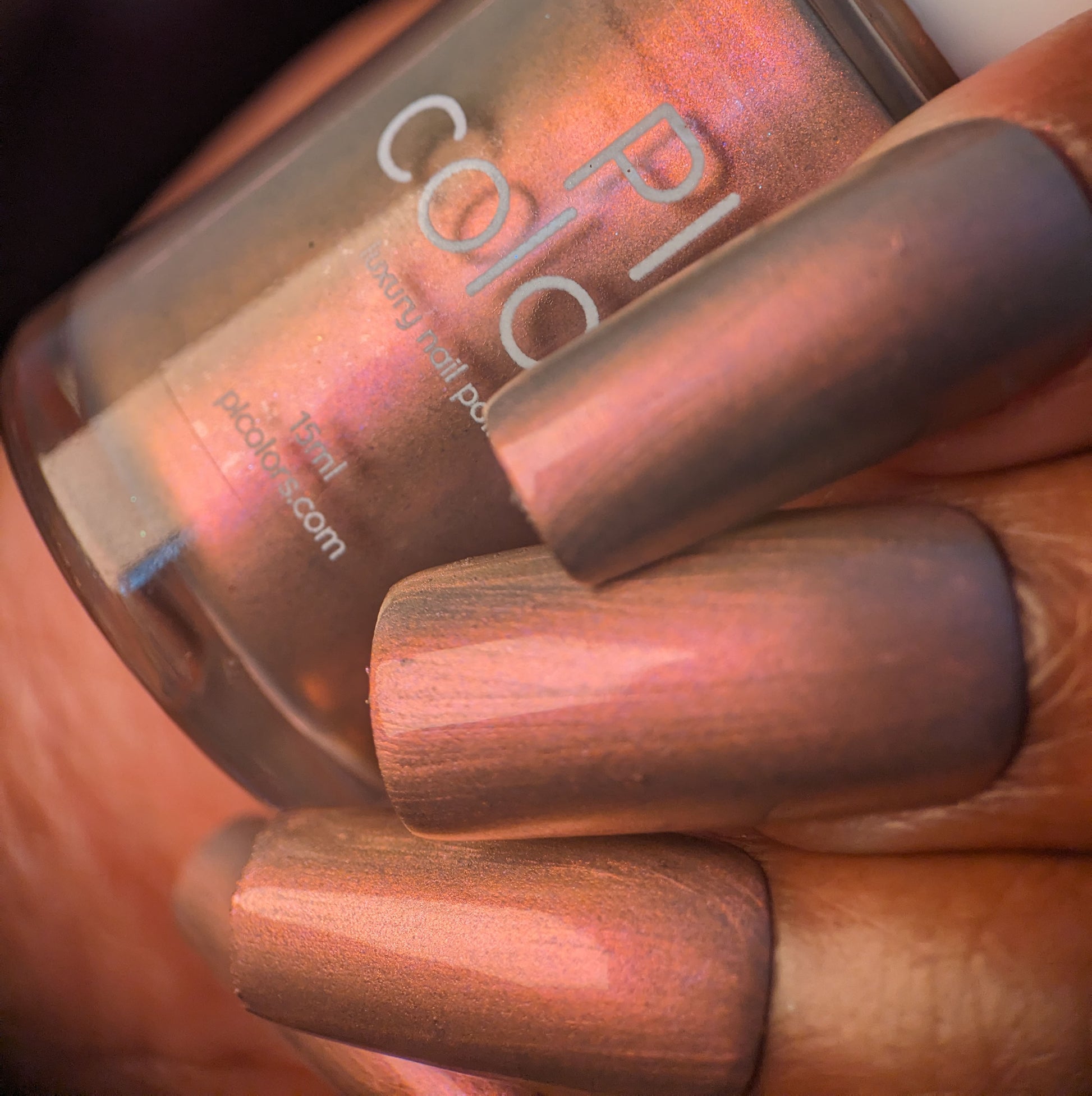 A close-up of a hand with long, shimmering nails painted in PI Colors' Mulberry Love.205 showcases luxury nail lacquers' allure. The hand gracefully holds the bottle, reflecting a gradient effect under light.