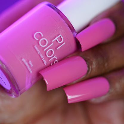 A close-up of a hand with long, square-shaped nails painted bright pink, holding a matching bottle of handmade PI Colors nail polish labeled "Neapolitan.432.