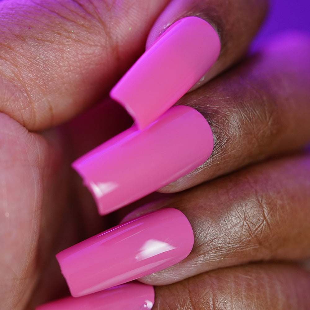 A close-up of a hand with long, glossy, cool-toned pink acrylic nails painted with PI Colors Neapolitan.432 creme polish, one showing a break at the tip. The neat manicure stands out against a blurred purple background.
