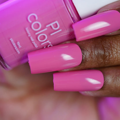 A close-up of a hand with long, manicured nails painted in glossy, cool-toned pink "Neapolitan.432" by PI Colors, holding a matching bottle of this handmade nail polish.