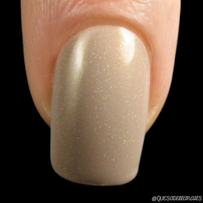 A close-up of a fingernail showcases the glossy finish of AuNaturale.016 Nude Nail Polish by PI Colors, with its nude holographic effect and subtle glittery specks. The black background highlights the shine and texture, elevating this 10-free nail polish to the elegance of luxury nail lacquers.