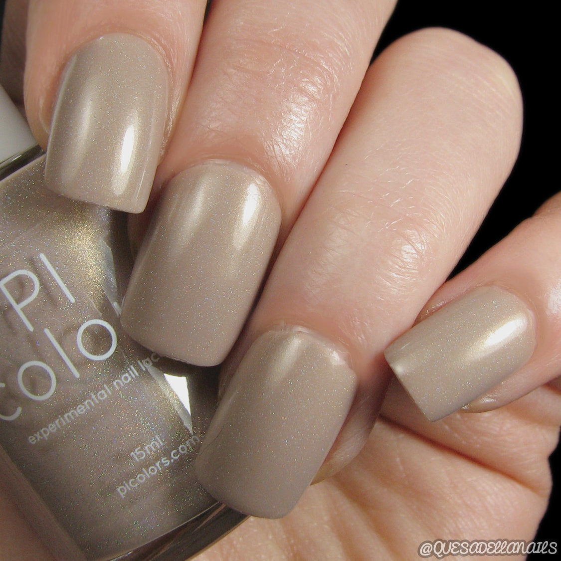 Fingers with short, neatly manicured nails are painted in AuNaturale.016 Nude Nail Polish by PI Colors, featuring a taupe hue with a subtle shimmer that exemplifies the elegance of luxury nail lacquers. A matching PI Colors nail polish bottle is held between the thumb and index finger.