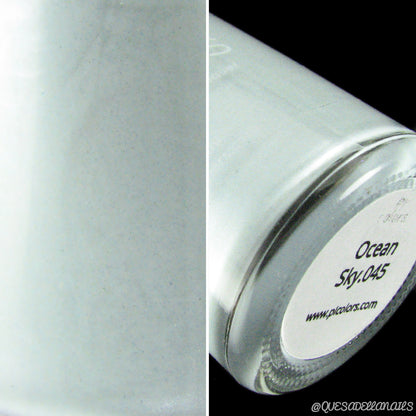 Close-up of a light gray, 10-free nail polish bottle from PI Colors. The left side displays the color, and the right reveals the bottom label reading "Ocean Sky.045" alongside a website URL. Set against a black background, this handmade nail polish exudes elegance and sophistication.