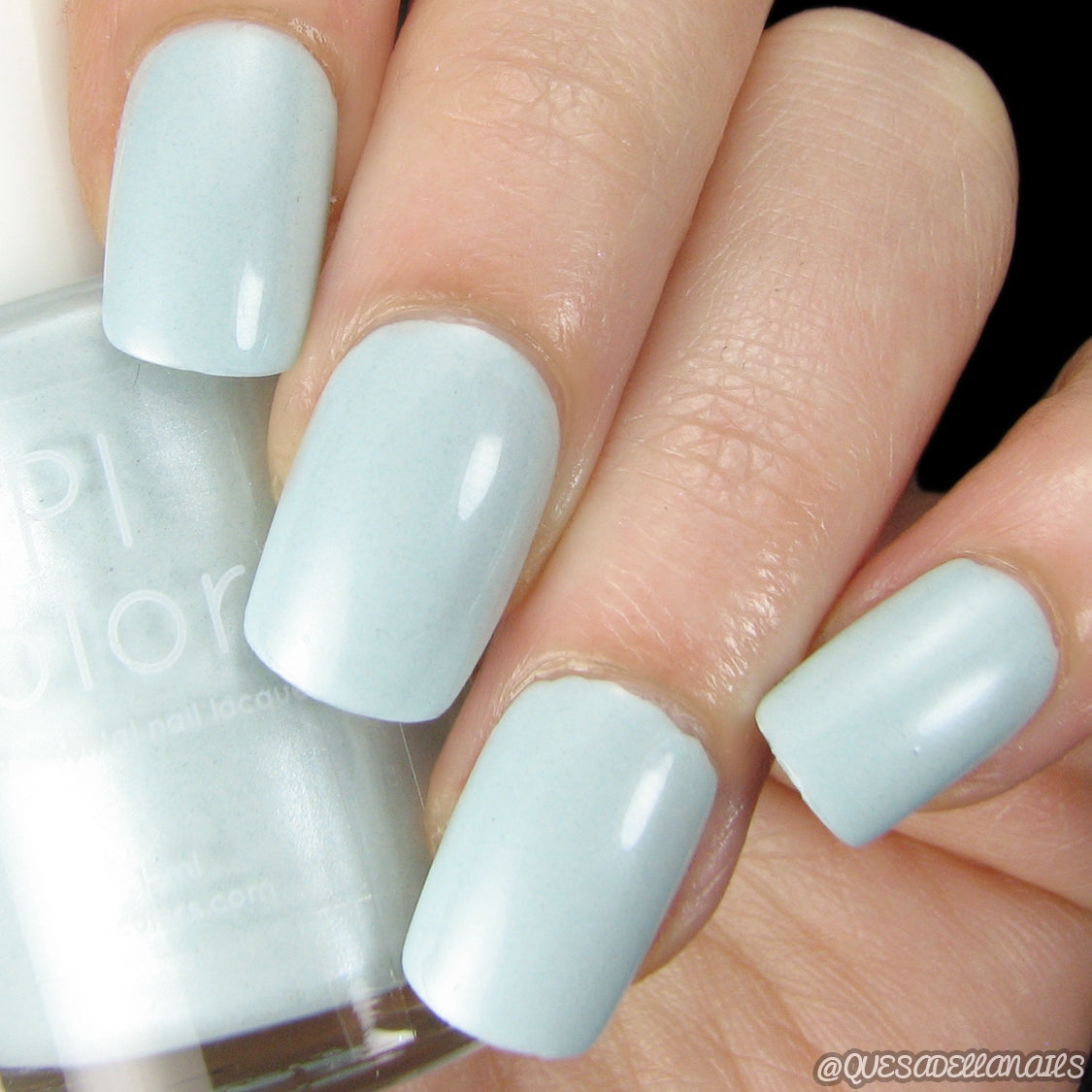 A hand with four fingernails painted in Ocean Sky.045, a soft pastel blue shade by PI Colors, holds a bottle of the same handmade, 10-free nail polish close to the fingers. The glossy finish provides an elegant touch.