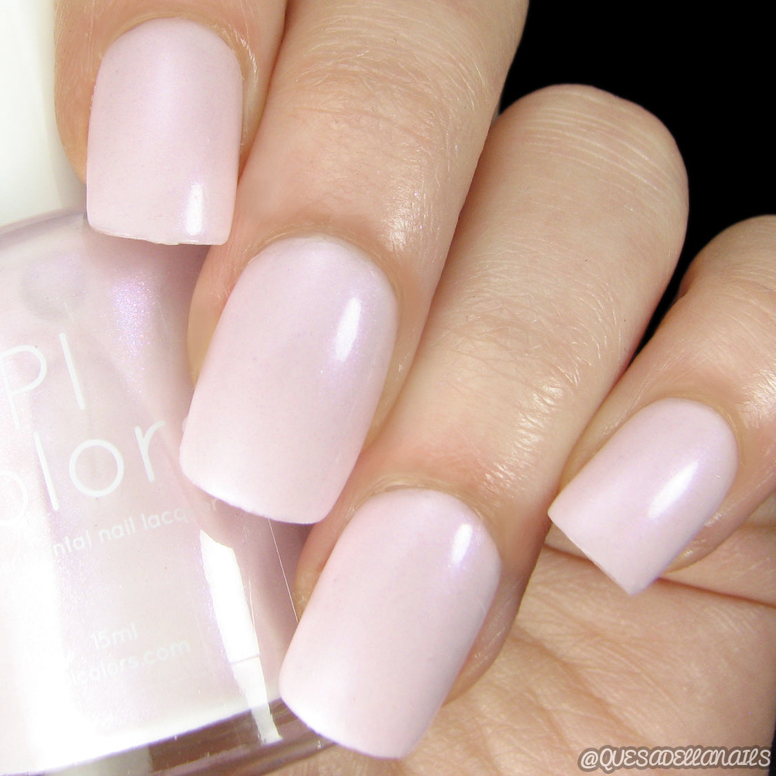 Close-up photo of a hand with nails painted in a soft, pastel pink shade using PI Colors' luxury nail lacquer, Pink.001 Pink Nail Polish. The polish bottle is partially visible, displaying the same color. The nails have a glossy finish and a smooth texture.