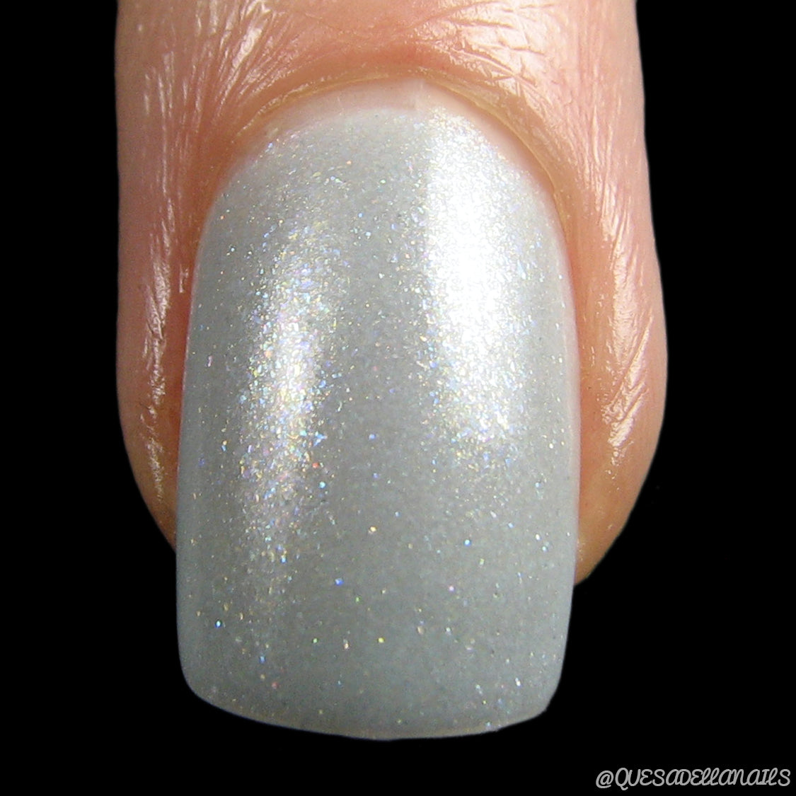 A close-up of a fingernail showcases the stunning Storm Morning.062 Blue Gray Nail Polish by PI Colors, adorned with holographic glitter for an opulent touch. The glossy finish and subtle sparkle captivate the eye, while the sharply focused image emphasizes the polished nail against visible skin.